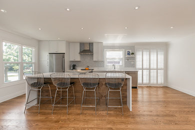 Eat-in kitchen - large transitional single-wall light wood floor eat-in kitchen idea in Toronto with an undermount sink, shaker cabinets, white cabinets, quartzite countertops, white backsplash, mosaic tile backsplash, stainless steel appliances and an island