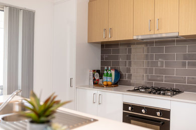 Foto på ett mellanstort funkis vit kök med öppen planlösning, med en dubbel diskho, skåp i ljust trä, granitbänkskiva, grått stänkskydd, stänkskydd i keramik, rostfria vitvaror, ljust trägolv och en köksö