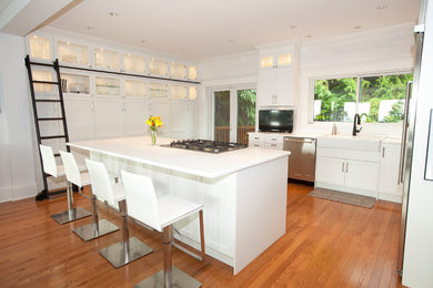 Example of a mid-sized trendy u-shaped medium tone wood floor and brown floor eat-in kitchen design in Vancouver with a farmhouse sink, shaker cabinets, white cabinets, quartzite countertops, white backsplash, ceramic backsplash, stainless steel appliances and an island
