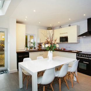Contemporary l-shaped kitchen/diner in London with a built-in sink, flat-panel cabinets, white cabinets, wood worktops, white splashback, metro tiled splashback, black appliances, no island, beige floors and brown worktops.