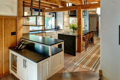 Urban l-shaped light wood floor and gray floor kitchen photo in Other with a farmhouse sink, beaded inset cabinets, white cabinets, soapstone countertops, multicolored backsplash, mosaic tile backsplash, paneled appliances, an island and black countertops