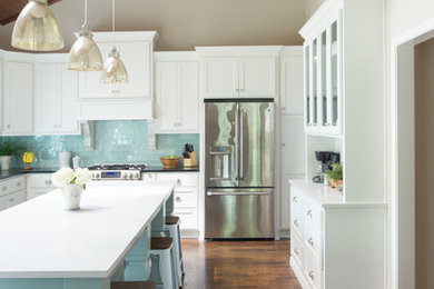Inspiration for a mid-sized timeless u-shaped medium tone wood floor enclosed kitchen remodel in Kansas City with a farmhouse sink, flat-panel cabinets, white cabinets, quartz countertops, blue backsplash, glass tile backsplash, stainless steel appliances and an island