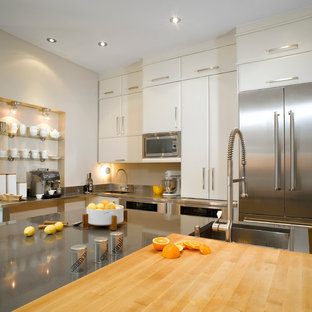 Idées déco pour une grand cuisine américaine moderne en L avec un électroménager en acier inoxydable, un évier encastré, un placard à porte plane, des portes de placard blanches, un plan de travail en quartz modifié, une crédence métallisée, une crédence en dalle métallique, un sol en bois clair et un îlot central.