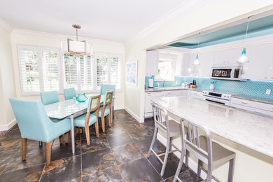 Inspiration for a medium sized coastal single-wall kitchen/diner in Miami with a submerged sink, flat-panel cabinets, white cabinets, granite worktops, blue splashback, glass tiled splashback, white appliances and a breakfast bar.