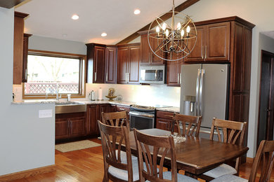 Eat-in kitchen - mid-sized transitional l-shaped medium tone wood floor and brown floor eat-in kitchen idea in Other with a farmhouse sink, white backsplash, subway tile backsplash, stainless steel appliances, raised-panel cabinets, dark wood cabinets and granite countertops