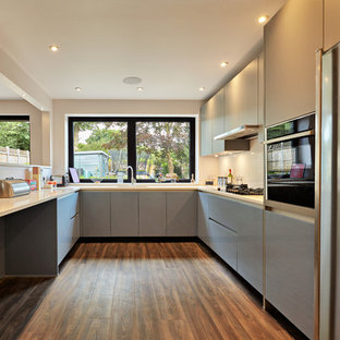 This is an example of a contemporary u-shaped kitchen in Essex with flat-panel cabinets, grey cabinets, beige splashback, stainless steel appliances, dark hardwood flooring, a breakfast bar, brown floors and beige worktops.