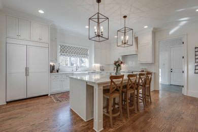 Design ideas for a large traditional l-shaped kitchen in Nashville with a belfast sink, recessed-panel cabinets, white cabinets, engineered stone countertops, white splashback, porcelain splashback, integrated appliances, medium hardwood flooring, an island and brown floors.
