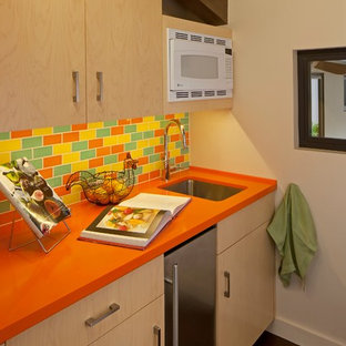 Foto de cocina lineal, retro, pequeña, cerrada, con fregadero bajoencimera, armarios con paneles lisos, puertas de armario de madera clara, encimera de acrílico, salpicadero multicolor, salpicadero de azulejos de cerámica, electrodomésticos de acero inoxidable, suelo de madera oscura y encimeras naranjas