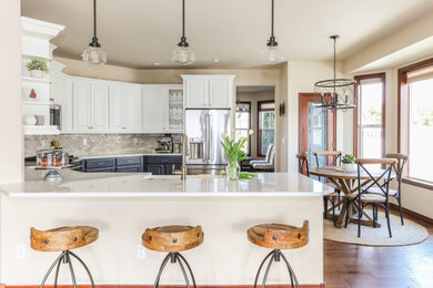 Example of a mid-sized transitional u-shaped medium tone wood floor and brown floor eat-in kitchen design in Seattle with a farmhouse sink, white cabinets, quartz countertops, gray backsplash, marble backsplash, stainless steel appliances, white countertops, raised-panel cabinets and a peninsula