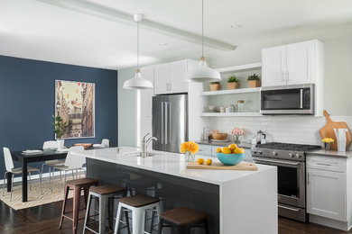 Example of a large trendy single-wall medium tone wood floor eat-in kitchen design in Boston with a drop-in sink, shaker cabinets, white cabinets, quartz countertops, white backsplash, subway tile backsplash, stainless steel appliances and an island