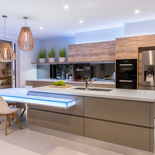Mid-sized contemporary galley open plan kitchen in Brisbane with a double-bowl sink, flat-panel cabinets, glass benchtops, mirror splashback, beige floor, medium wood cabinets, black appliances, with island and grey benchtop.