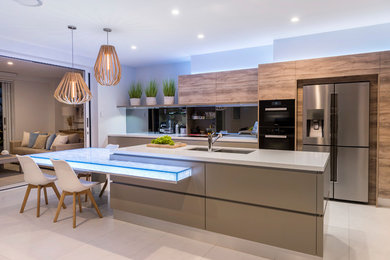 Example of a mid-sized trendy galley beige floor open concept kitchen design in Brisbane with a double-bowl sink, flat-panel cabinets, glass countertops, mirror backsplash, medium tone wood cabinets, black appliances, an island and gray countertops