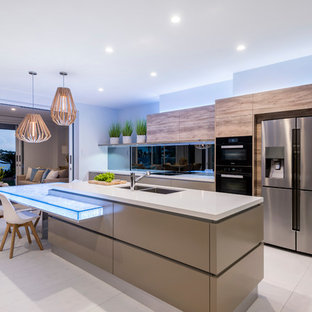 Large contemporary galley open plan kitchen in Brisbane with a double-bowl sink, flat-panel cabinets, cement tiles, with island, beige floor, beige benchtop, medium wood cabinets, black splashback and stainless steel appliances.
