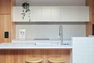 メルボルンにある北欧スタイルのおしゃれなキッチン (アンダーカウンターシンク、フラットパネル扉のキャビネット、白いキャビネット、白いキッチンパネル、淡色無垢フローリング、白いキッチンカウンター) の写真