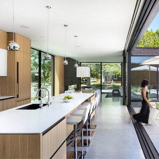 Idee per una cucina moderna con lavello sottopiano, ante lisce, ante in legno chiaro, paraspruzzi bianco, elettrodomestici da incasso, pavimento in cemento, isola, pavimento grigio e top bianco