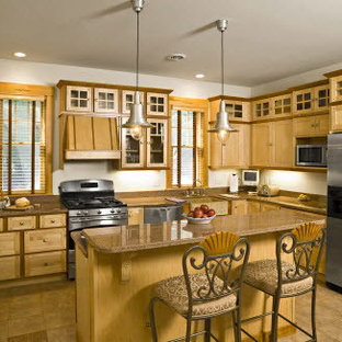 Mid-sized eclectic l-shaped kitchen in Portland Maine with a farmhouse sink, shaker cabinets, light wood cabinets, granite benchtops, stone slab splashback, stainless steel appliances, porcelain floors, with island and brown floor.