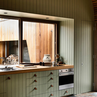 Photo of an industrial kitchen in Sydney with a drop-in sink, flat-panel cabinets, green cabinets, wood benchtops, stainless steel appliances, brown floor, brown benchtop, vaulted and wood.