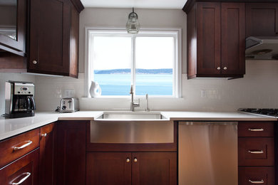 Example of a large transitional u-shaped medium tone wood floor and brown floor enclosed kitchen design in Seattle with a farmhouse sink, shaker cabinets, dark wood cabinets, solid surface countertops, white backsplash, subway tile backsplash, stainless steel appliances and a peninsula