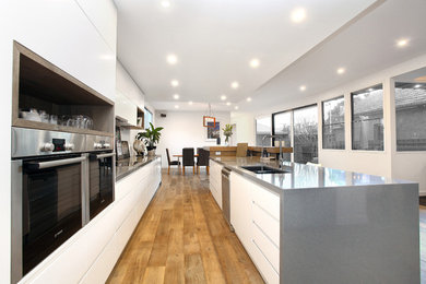 Imagen de cocina moderna abierta con puertas de armario blancas, encimera de cuarzo compacto y una isla