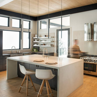 Immagine di una cucina a L rustica con lavello stile country, elettrodomestici in acciaio inossidabile, parquet chiaro, isola e top bianco