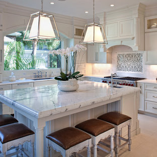 Foto di una cucina a L classica di medie dimensioni con lavello sottopiano, ante con riquadro incassato, ante bianche, paraspruzzi bianco, elettrodomestici in acciaio inossidabile, isola e pavimento con piastrelle in ceramica