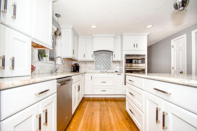 Example of a l-shaped medium tone wood floor kitchen design in Boston with white cabinets, granite countertops, gray backsplash, subway tile backsplash, stainless steel appliances, an island and multicolored countertops