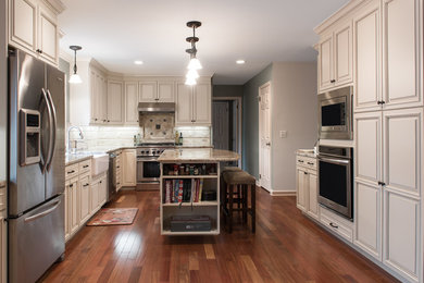 Example of a large classic u-shaped medium tone wood floor and brown floor eat-in kitchen design in New York with an island, a farmhouse sink, raised-panel cabinets, beige cabinets, granite countertops, beige backsplash, stone tile backsplash and stainless steel appliances