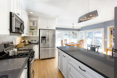 Eat-in kitchen - mid-sized transitional u-shaped light wood floor eat-in kitchen idea in Boston with an undermount sink, recessed-panel cabinets, white cabinets, gray backsplash, stone tile backsplash, stainless steel appliances and an island