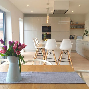Photo of a scandinavian l-shaped eat-in kitchen in London with flat-panel cabinets, light hardwood floors, with island, white benchtop, an integrated sink, grey cabinets, limestone benchtops, white splashback, limestone splashback, panelled appliances and white floor.