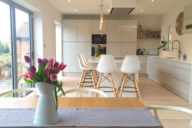 Photo of a scandinavian l-shaped kitchen/diner in London with flat-panel cabinets, light hardwood flooring, an island, white worktops, an integrated sink, grey cabinets, limestone worktops, white splashback, limestone splashback, integrated appliances and white floors.