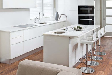 Eat-in kitchen - mid-sized contemporary l-shaped medium tone wood floor eat-in kitchen idea in Detroit with an undermount sink, flat-panel cabinets, white cabinets, quartz countertops, white backsplash, stone slab backsplash, paneled appliances and an island