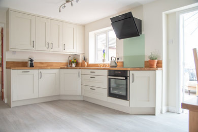 Design ideas for a large contemporary kitchen/diner in Sussex with shaker cabinets, white cabinets, wood worktops, black appliances, laminate floors and no island.