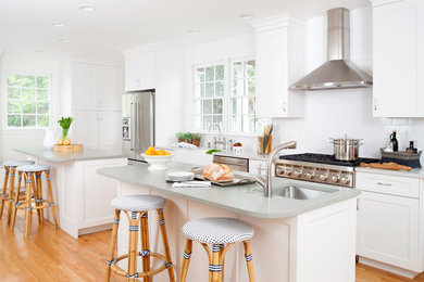 Example of a transitional galley light wood floor kitchen design in Baltimore with a farmhouse sink, shaker cabinets, white cabinets, white backsplash, subway tile backsplash, stainless steel appliances and two islands