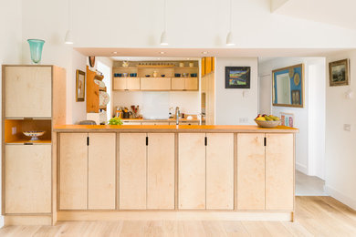 Medium sized scandi l-shaped open plan kitchen in Other with light wood cabinets, wood worktops, white splashback, glass sheet splashback, integrated appliances and a breakfast bar.