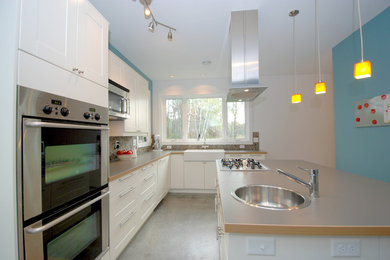 Open concept kitchen - mid-sized country u-shaped concrete floor open concept kitchen idea in Minneapolis with a farmhouse sink, shaker cabinets, white cabinets, laminate countertops, multicolored backsplash, glass tile backsplash and stainless steel appliances