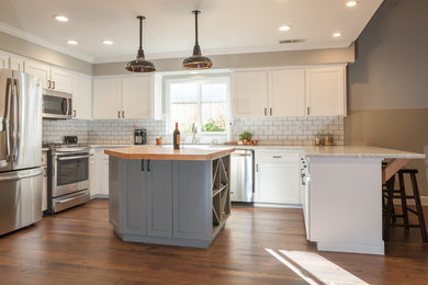 Example of a mid-sized country u-shaped dark wood floor eat-in kitchen design in Other with a farmhouse sink, shaker cabinets, white cabinets, marble countertops, white backsplash, subway tile backsplash, stainless steel appliances and an island