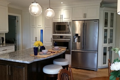 Example of a large trendy l-shaped light wood floor enclosed kitchen design in Other with a single-bowl sink, raised-panel cabinets, white cabinets, granite countertops, white backsplash, subway tile backsplash, stainless steel appliances, an island and multicolored countertops