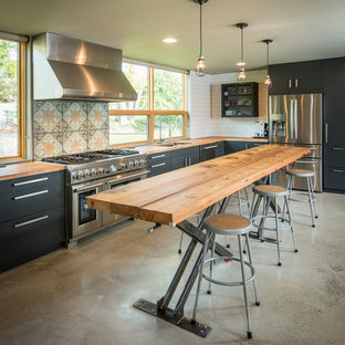 Mid-sized industrial eat-in kitchen ideas - Eat-in kitchen - mid-sized industrial l-shaped concrete floor eat-in kitchen idea in Philadelphia with an undermount sink, flat-panel cabinets, black cabinets, wood countertops, white backsplash, subway tile backsplash, stainless steel appliances and an island