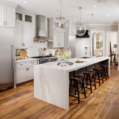 Example of a mid-sized transitional galley medium tone wood floor and brown floor open concept kitchen design in Houston with a farmhouse sink, shaker cabinets, gray cabinets, white backsplash, stainless steel appliances, an island, quartz countertops and white countertops