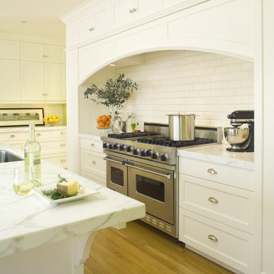 Example of a mid-sized classic l-shaped medium tone wood floor eat-in kitchen design in San Francisco with stainless steel appliances, subway tile backsplash, an undermount sink, recessed-panel cabinets, white cabinets, marble countertops, white backsplash and an island