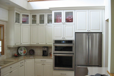 Example of a mid-sized classic l-shaped dark wood floor and brown floor enclosed kitchen design in Denver with a double-bowl sink, raised-panel cabinets, white cabinets, solid surface countertops, beige backsplash, ceramic backsplash and stainless steel appliances