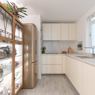 This is an example of a small contemporary galley enclosed kitchen in Sussex with no island, a submerged sink, flat-panel cabinets, white cabinets, white splashback, stone slab splashback, coloured appliances, beige floors and white worktops.