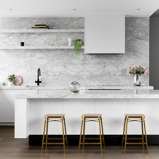 Photo of a contemporary galley kitchen in Melbourne with an undermount sink, flat-panel cabinets, white cabinets, marble benchtops, white splashback, marble splashback, black appliances, medium hardwood floors, with island, brown floor and white benchtop.