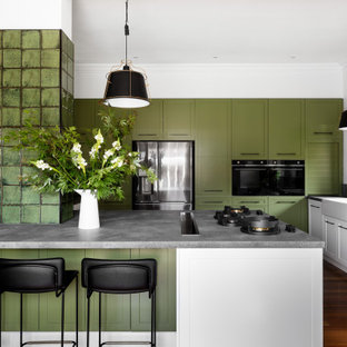 Photo of a contemporary l-shaped kitchen in Melbourne with a farmhouse sink, shaker cabinets, white cabinets, black appliances, dark hardwood floors, a peninsula, brown floor and grey benchtop.