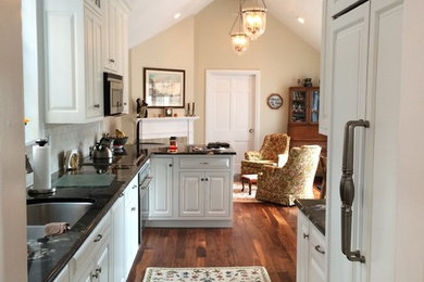Example of a mid-sized transitional galley medium tone wood floor open concept kitchen design in Philadelphia with an undermount sink, raised-panel cabinets, white cabinets, granite countertops, gray backsplash, subway tile backsplash, paneled appliances and a peninsula