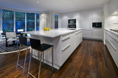 Example of a large trendy l-shaped dark wood floor eat-in kitchen design in Atlanta with an undermount sink, flat-panel cabinets, white cabinets, quartz countertops, glass sheet backsplash, stainless steel appliances, an island and white backsplash