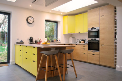 Photo of a medium sized retro u-shaped open plan kitchen in Other with a built-in sink, flat-panel cabinets, yellow cabinets, concrete worktops, stainless steel appliances, ceramic flooring, a breakfast bar, grey floors and grey worktops.