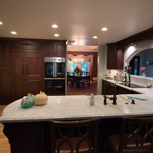 Mid-sized traditional kitchen remodeling - Kitchen - mid-sized traditional u-shaped porcelain tile and brown floor kitchen idea in Other with a farmhouse sink, recessed-panel cabinets, dark wood cabinets, quartz countertops, gray backsplash, mosaic tile backsplash, paneled appliances and white countertops