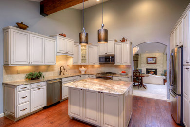 Example of a large classic l-shaped medium tone wood floor enclosed kitchen design in Denver with an undermount sink, granite countertops, beige backsplash, stone tile backsplash, stainless steel appliances, an island, raised-panel cabinets and beige cabinets