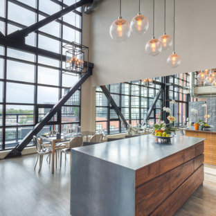 This is an example of a mid-sized modern galley open plan kitchen in Toronto with flat-panel cabinets, medium wood cabinets, zinc benchtops, brown splashback, stone slab splashback, black appliances, light hardwood floors, with island and beige floor.